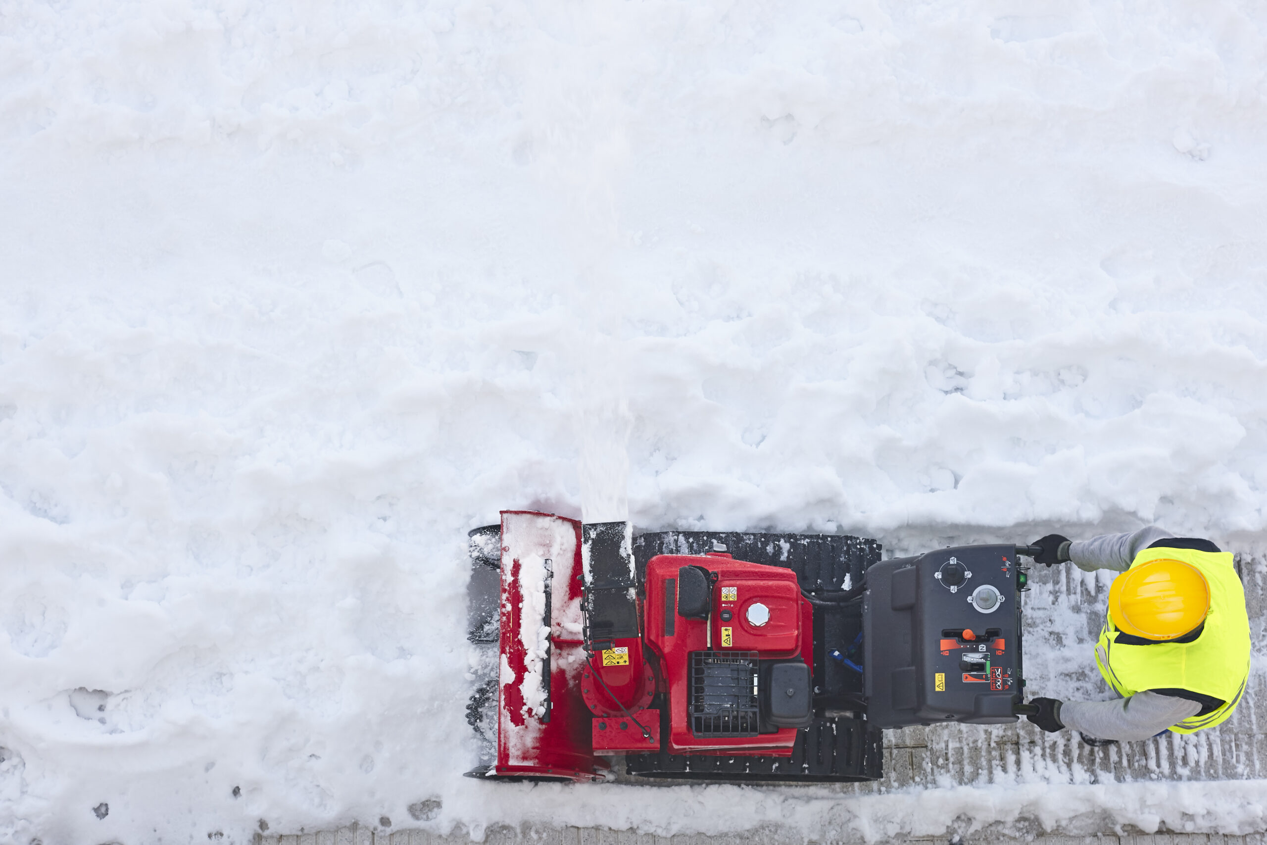 Top down view of a worker clearing thick snow beside a red machine.