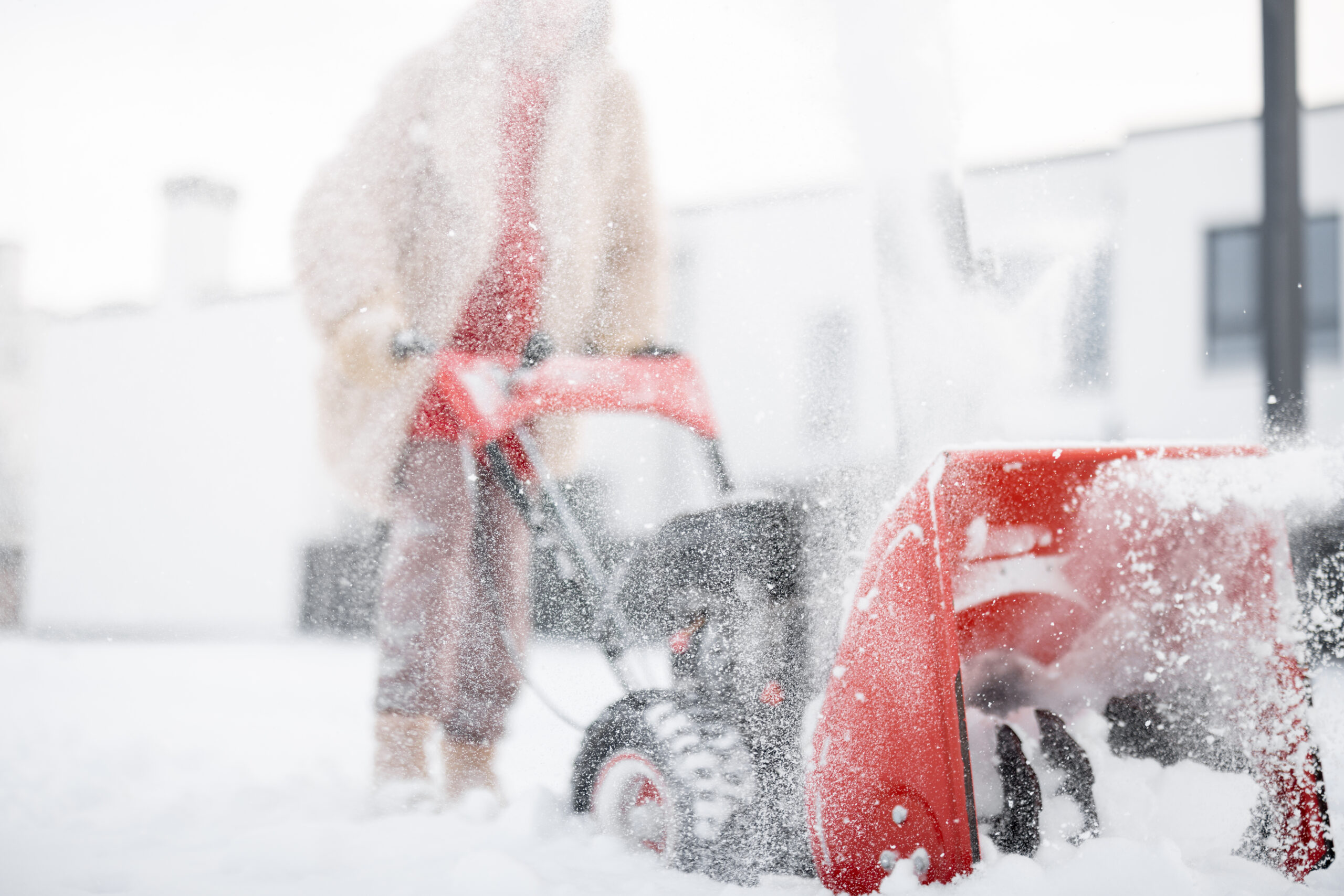 Snow blower throws heavy snow while a worker operates it in winter.